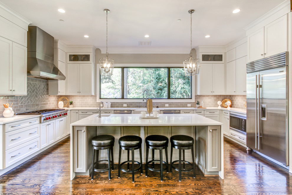 Photo of a traditional u-shaped kitchen in DC Metro with a farmhouse sink, shaker cabinets, white cabinets, grey splashback, subway tile splashback, stainless steel appliances, medium hardwood floors and with island.