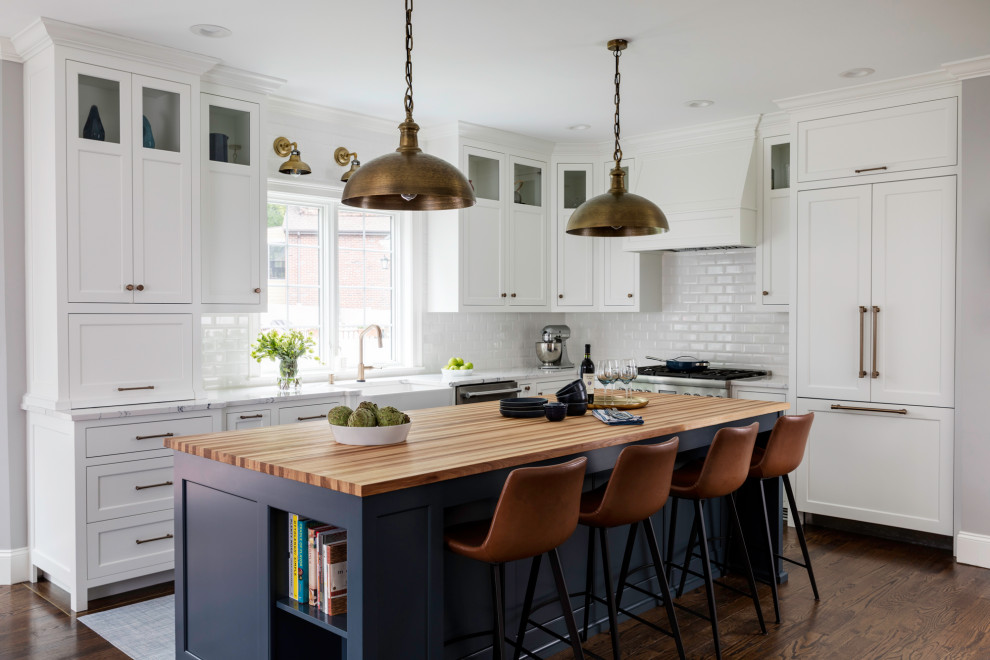 This is an example of a mid-sized transitional l-shaped eat-in kitchen in Boston with a farmhouse sink, recessed-panel cabinets, white cabinets, quartzite benchtops, white splashback, subway tile splashback, stainless steel appliances, medium hardwood floors, with island and white benchtop.