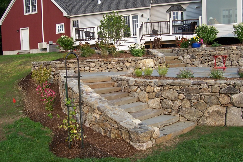 Large country backyard full sun garden in Manchester with a retaining wall and natural stone pavers for summer.