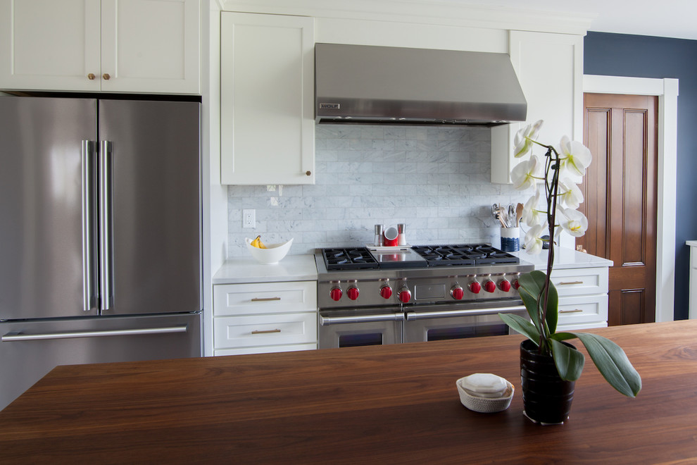 Inspiration for a large transitional l-shaped enclosed kitchen remodel in Boston with a farmhouse sink, shaker cabinets, white cabinets, quartz countertops, white backsplash, stainless steel appliances, an island and white countertops