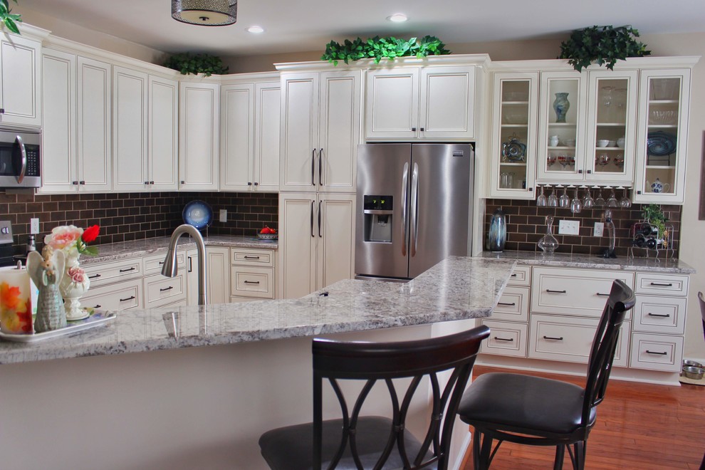 Inspiration for a mid-sized u-shaped medium tone wood floor and brown floor kitchen remodel in Charleston with an undermount sink, raised-panel cabinets, beige cabinets, granite countertops, brown backsplash, ceramic backsplash, stainless steel appliances and beige countertops