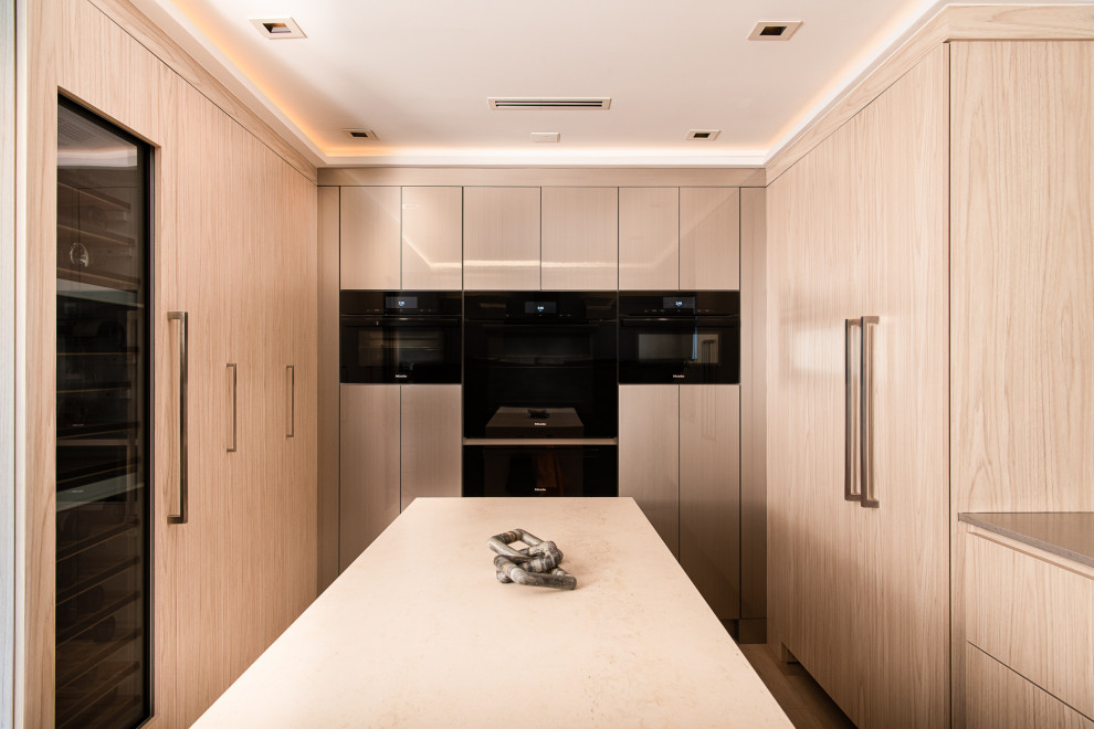 Modern inredning av ett brun brunt kök, med en undermonterad diskho, släta luckor, skåp i ljust trä, bänkskiva i kvartsit, beige stänkskydd, stänkskydd i porslinskakel, svarta vitvaror, vinylgolv, en köksö och brunt golv