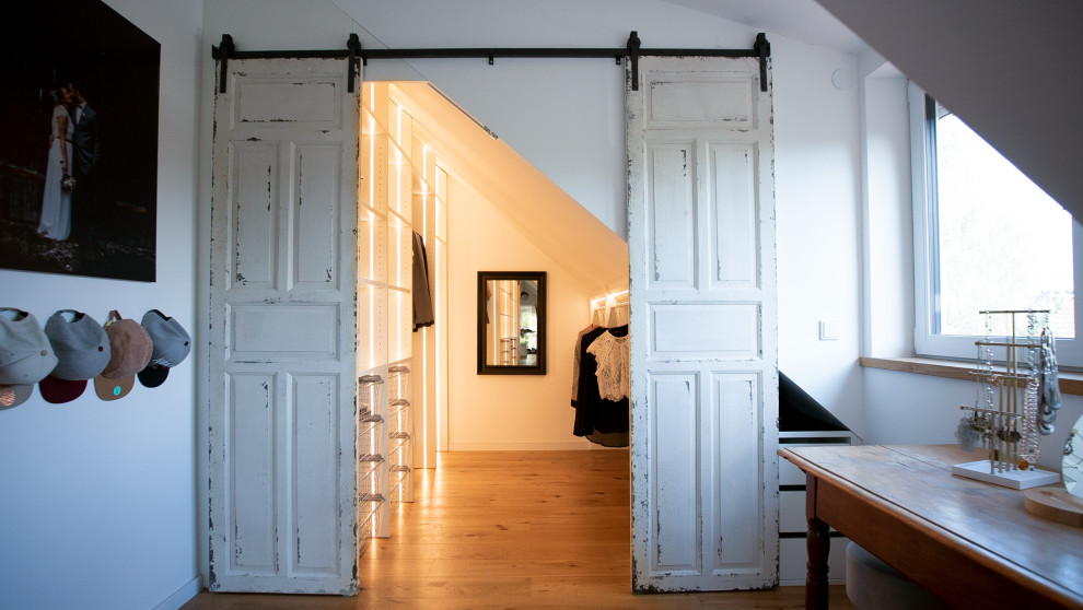 Diseño de armario vestidor escandinavo de tamaño medio con puertas de armario blancas, suelo de madera clara y suelo marrón