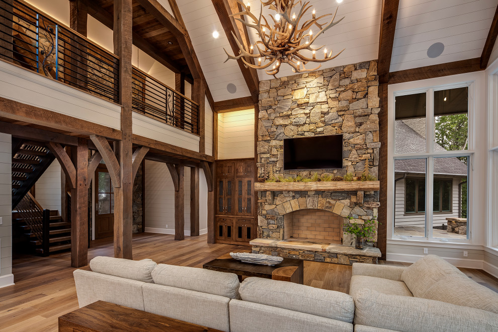 Large arts and crafts open concept living room in Other with grey walls, medium hardwood floors, a standard fireplace, a stone fireplace surround, a wall-mounted tv, grey floor, timber and planked wall panelling.