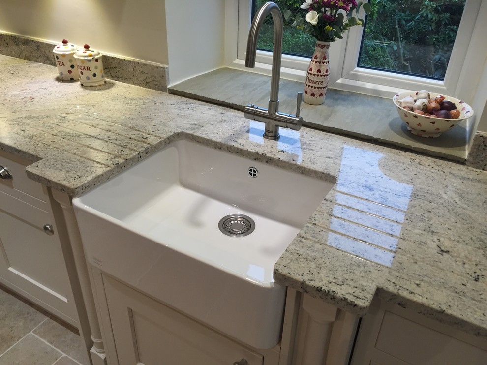 Large traditional l-shaped eat-in kitchen in Manchester with a farmhouse sink, recessed-panel cabinets, beige cabinets, granite benchtops, stainless steel appliances, limestone floors and with island.