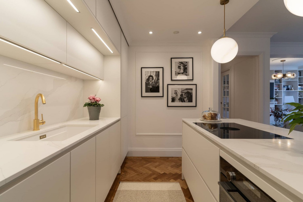 Inspiration for a medium sized contemporary single-wall open plan kitchen in Oxfordshire with a single-bowl sink, flat-panel cabinets, white cabinets, quartz worktops, white splashback, integrated appliances, medium hardwood flooring, an island, brown floors and white worktops.