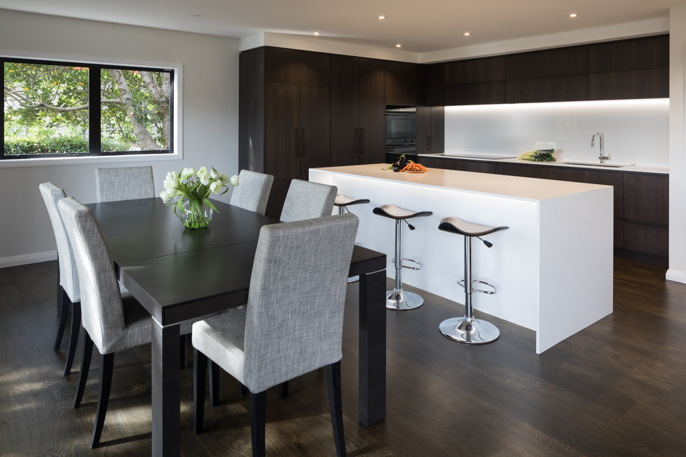 Photo of a Mid-sized contemporary Galley open plan kitchen in Auckland With an Undermount Sink, Flat-panel Cabinets, Medium Wood Cabinets, Quartz Benchtops, White Splashback, Stone Tile Splashback, Black Appliances, Dark Hardwood Floors, with Island, Brown Floor and White Benchtop.
