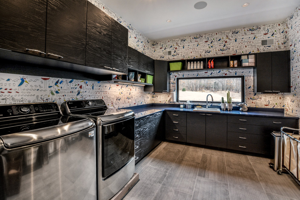 Photo of a large contemporary l-shaped dedicated laundry room in Other with a drop-in sink, flat-panel cabinets, black cabinets, quartz benchtops, multi-coloured walls, porcelain floors, a side-by-side washer and dryer and grey floor.