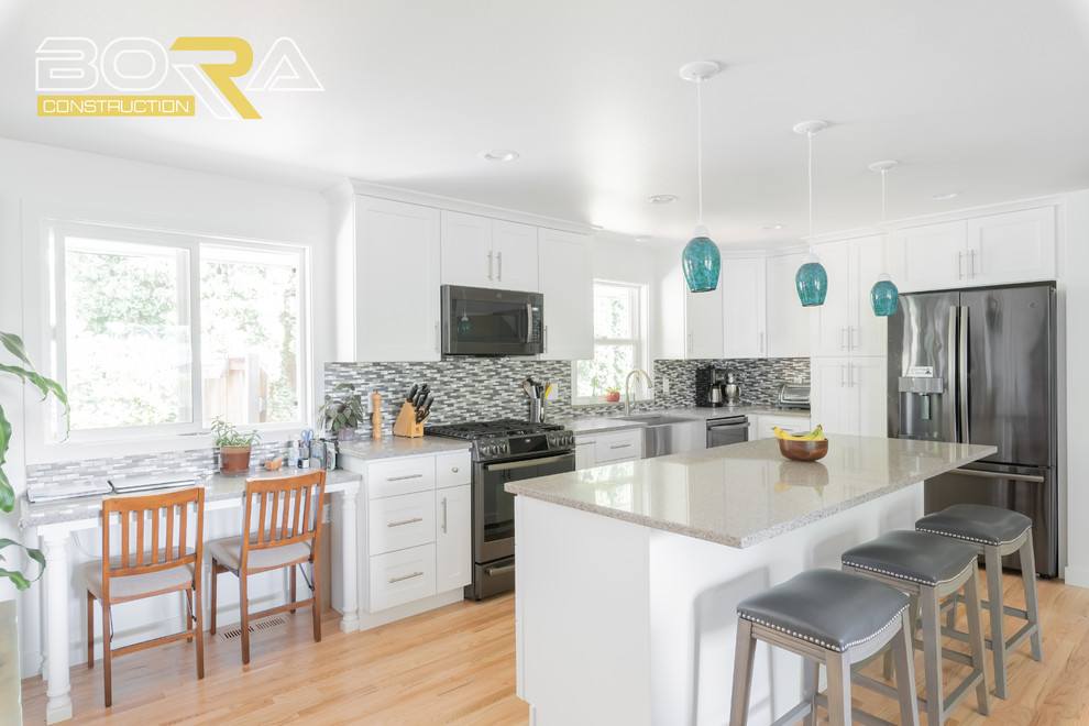 Inspiration for a mid-sized transitional l-shaped medium tone wood floor and brown floor eat-in kitchen remodel in Seattle with a farmhouse sink, shaker cabinets, white cabinets, quartz countertops, gray backsplash, ceramic backsplash, black appliances, an island and gray countertops
