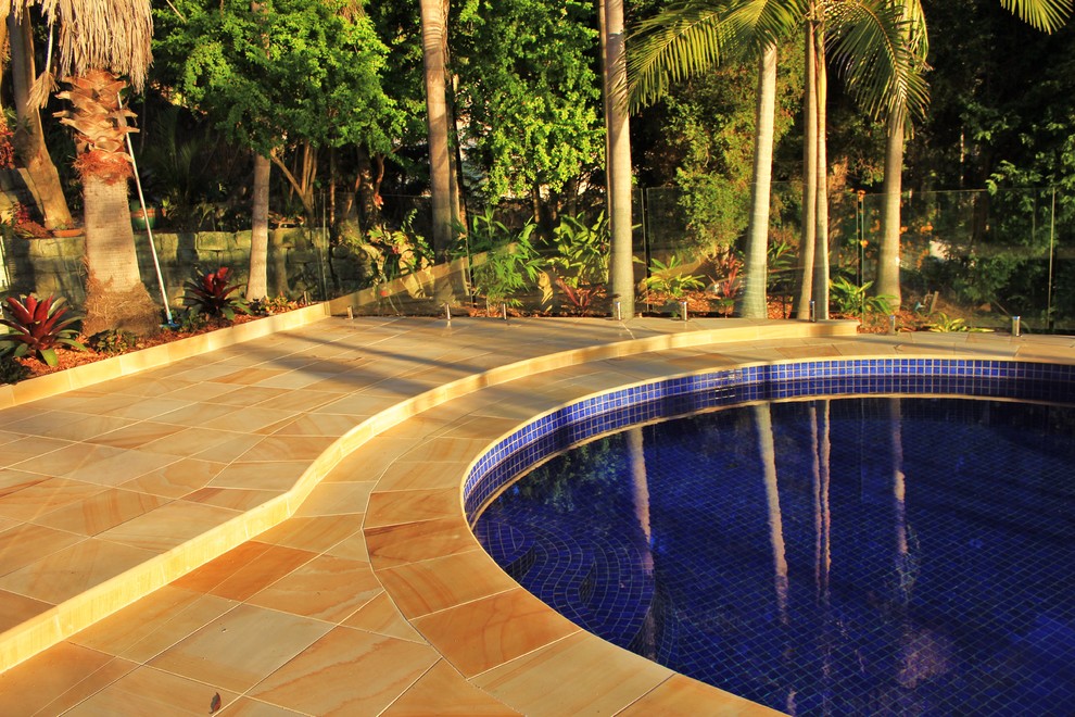 This is an example of a contemporary backyard custom-shaped pool in Sydney with natural stone pavers.