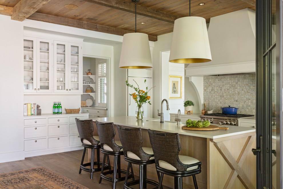 Klassisk inredning av ett vit vitt kök, med en rustik diskho, skåp i shakerstil, vita skåp, bänkskiva i kvarts, flerfärgad stänkskydd, integrerade vitvaror, mellanmörkt trägolv, en köksö och brunt golv
