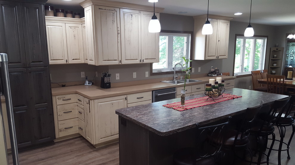 This is an example of a mid-sized country l-shaped eat-in kitchen in Minneapolis with a double-bowl sink, raised-panel cabinets, distressed cabinets, laminate benchtops, grey splashback, stainless steel appliances, vinyl floors and with island.
