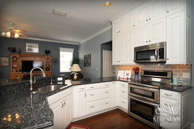 Mid-sized transitional u-shaped dark wood floor open concept kitchen photo in Orlando with a double-bowl sink, raised-panel cabinets, white cabinets, granite countertops, beige backsplash, subway tile backsplash and stainless steel appliances