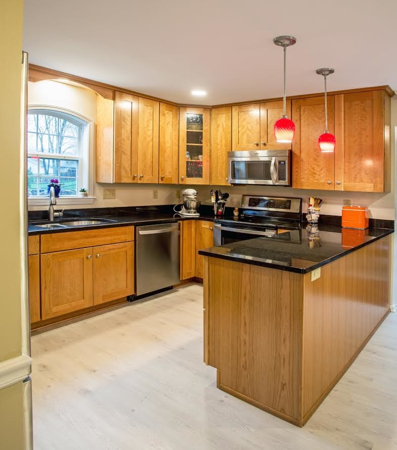 Design ideas for a traditional u-shaped eat-in kitchen in Baltimore with a double-bowl sink, shaker cabinets, medium wood cabinets, granite benchtops, stainless steel appliances, vinyl floors, a peninsula, grey floor and black benchtop.