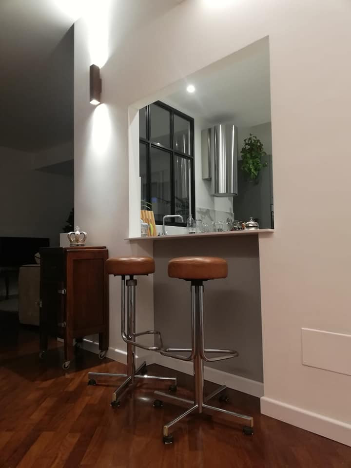 Design ideas for a large modern l-shaped seated home bar in Rome with flat-panel cabinets, grey cabinets, solid surface benchtops, white splashback, painted wood floors, brown floor and white benchtop.