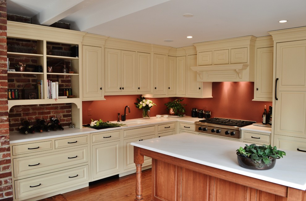 This is an example of a mid-sized traditional l-shaped eat-in kitchen in DC Metro with beaded inset cabinets, beige cabinets, marble benchtops, stainless steel appliances, medium hardwood floors, with island, an undermount sink and orange splashback.