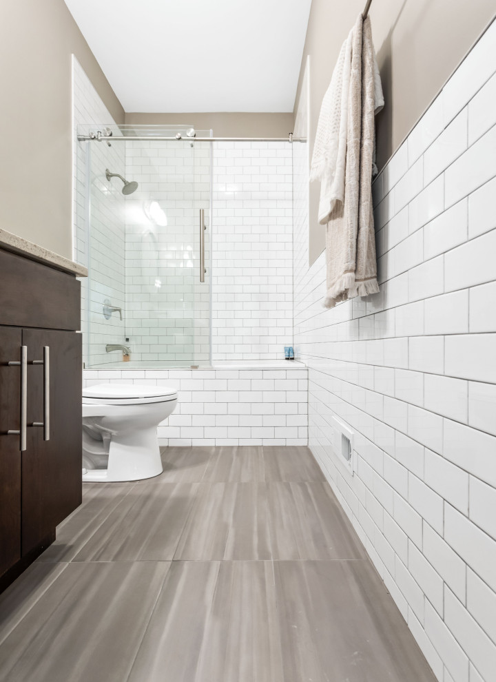 Photo of a mid-sized contemporary master bathroom in Chicago with flat-panel cabinets, brown cabinets, a shower/bathtub combo, a one-piece toilet, white tile, white walls, an undermount sink, engineered quartz benchtops, brown floor, a sliding shower screen, white benchtops, a double vanity and a built-in vanity.