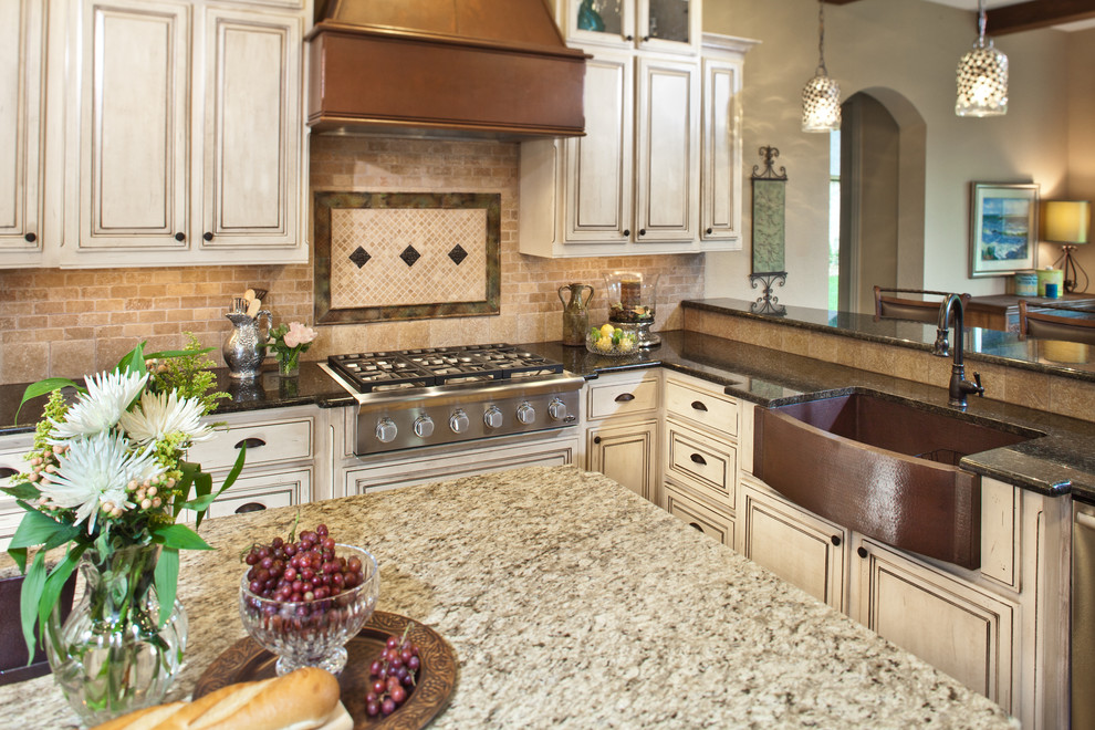 Inspiration for a mid-sized traditional u-shaped eat-in kitchen in Houston with a farmhouse sink, raised-panel cabinets, granite benchtops, beige splashback, stone tile splashback, stainless steel appliances, travertine floors and with island.
