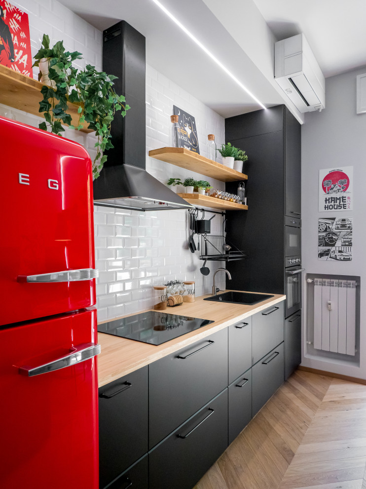 Small industrial single-wall open plan kitchen in Milan with a single-bowl sink, flat-panel cabinets, black cabinets, wood benchtops, white splashback, subway tile splashback, black appliances, light hardwood floors, no island and recessed.