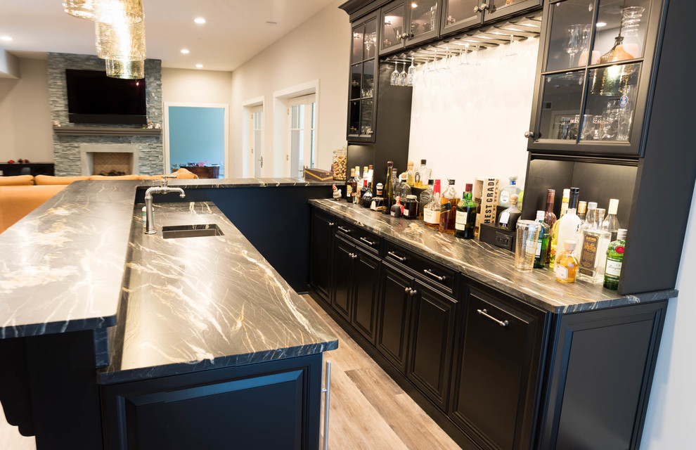 This is an example of a large transitional l-shaped seated home bar in Philadelphia with an undermount sink, raised-panel cabinets, black cabinets, soapstone benchtops, medium hardwood floors and brown floor.