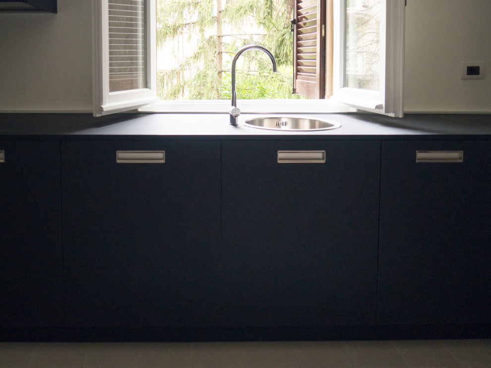 This is an example of a small midcentury l-shaped separate kitchen in Bologna with a drop-in sink, flat-panel cabinets, black cabinets, laminate benchtops, white splashback, black appliances, cement tiles, no island, white floor and black benchtop.
