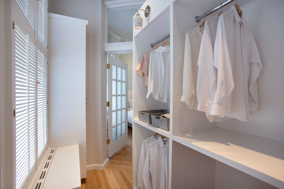 Inspiration for a mid-sized transitional gender-neutral walk-in wardrobe in Boston with flat-panel cabinets, white cabinets and light hardwood floors.