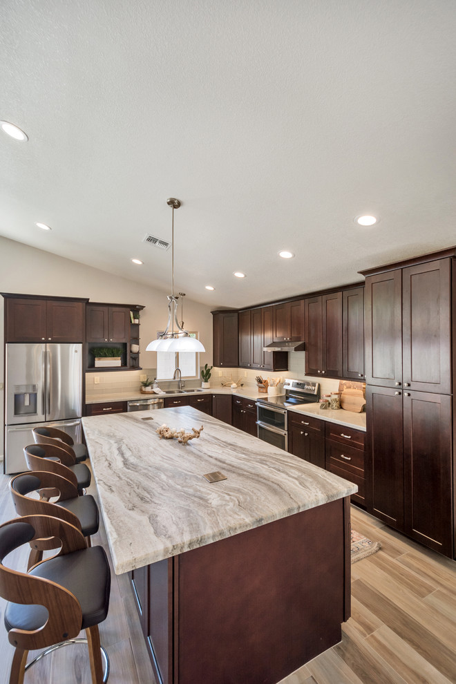 Inspiration for a mid-sized transitional l-shaped porcelain tile and brown floor open concept kitchen remodel in Phoenix with an undermount sink, shaker cabinets, brown cabinets, granite countertops, gray backsplash, glass tile backsplash, stainless steel appliances, an island and multicolored countertops