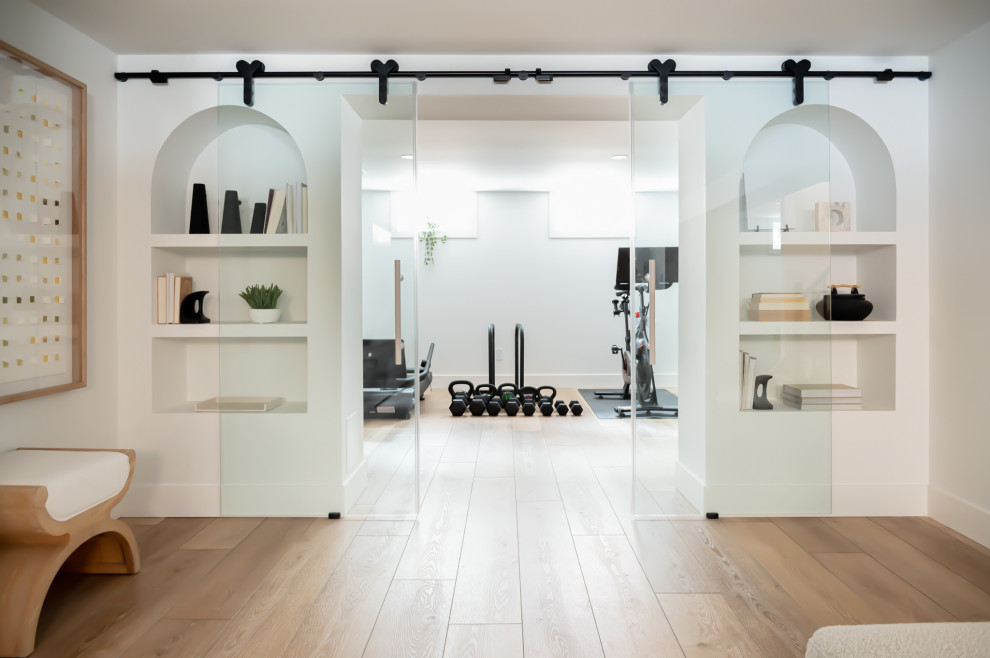 Example of a mid-sized danish medium tone wood floor multiuse home gym design in Toronto with white walls