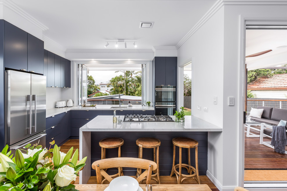 Photo of a small transitional l-shaped eat-in kitchen in Brisbane with an undermount sink, flat-panel cabinets, blue cabinets, quartz benchtops, white splashback, subway tile splashback, black appliances, medium hardwood floors, with island, brown floor and white benchtop.