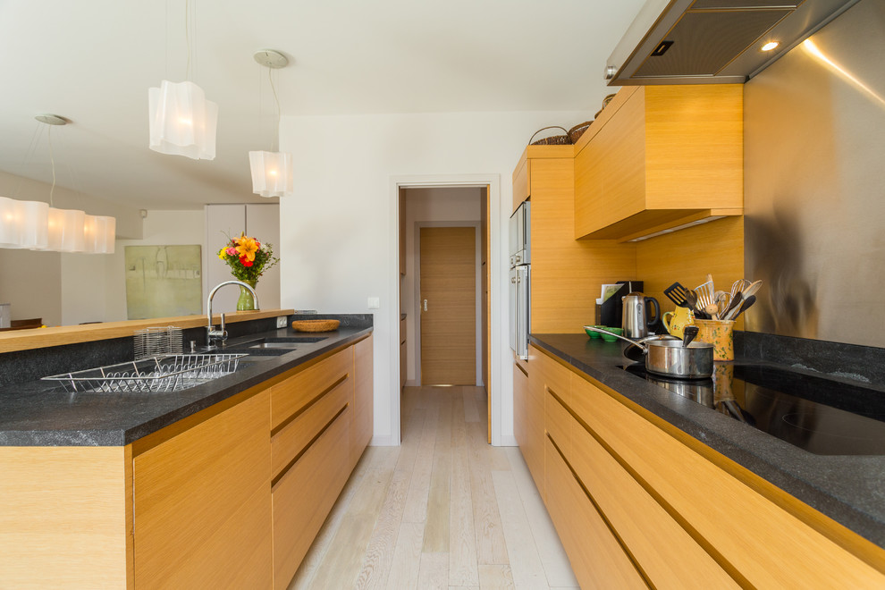 Design ideas for a mid-sized contemporary galley open plan kitchen in Nice with a double-bowl sink, flat-panel cabinets, medium wood cabinets, metallic splashback, metal splashback, light hardwood floors and a peninsula.