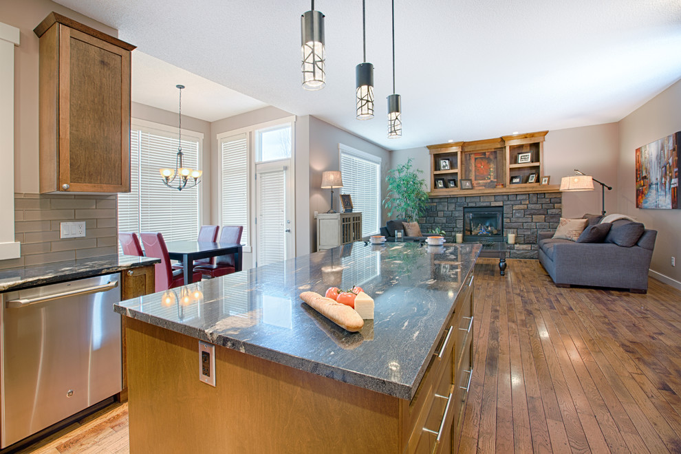 Example of a mid-sized mountain style u-shaped medium tone wood floor and brown floor eat-in kitchen design in Calgary with an undermount sink, shaker cabinets, medium tone wood cabinets, granite countertops, gray backsplash, glass tile backsplash, stainless steel appliances and an island