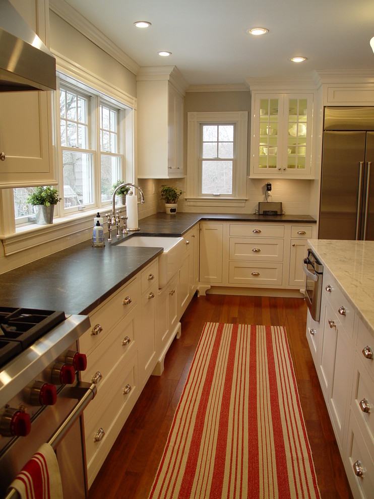 Enclosed kitchen - transitional enclosed kitchen idea in Boston with a farmhouse sink, recessed-panel cabinets, white cabinets, granite countertops, white backsplash, subway tile backsplash, stainless steel appliances and an island