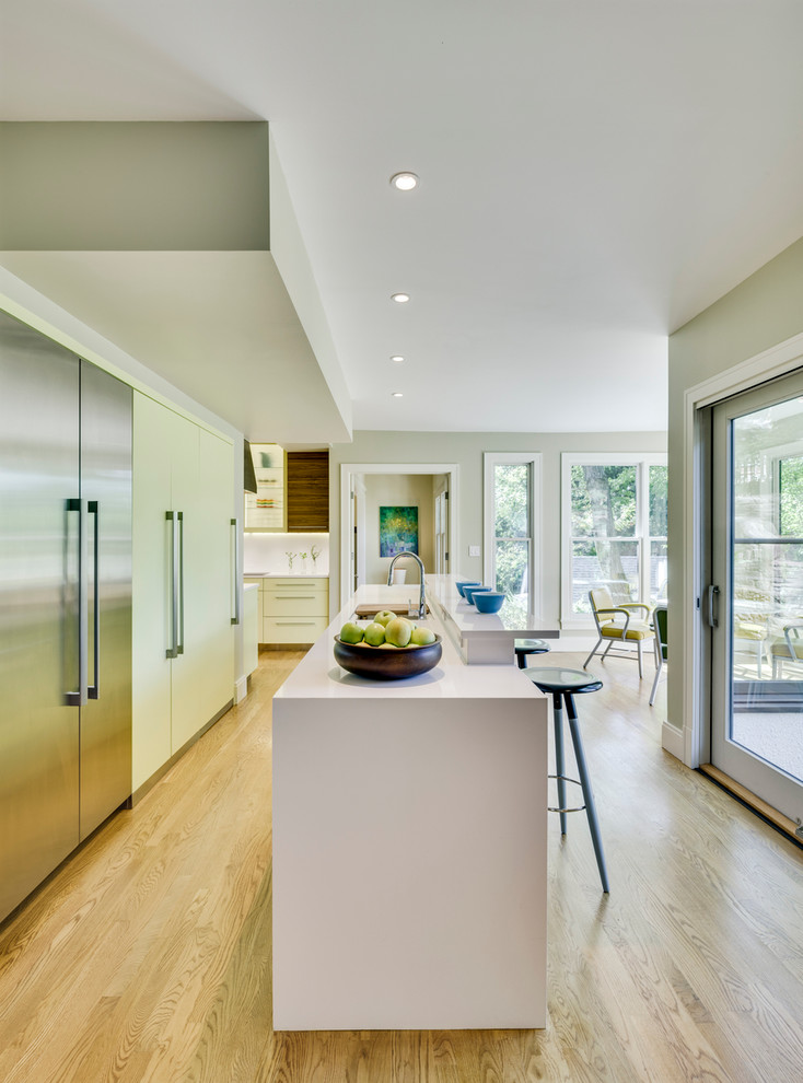Large modern open plan kitchen in New York with an undermount sink, flat-panel cabinets, yellow cabinets, white splashback, glass sheet splashback, stainless steel appliances, light hardwood floors and with island.