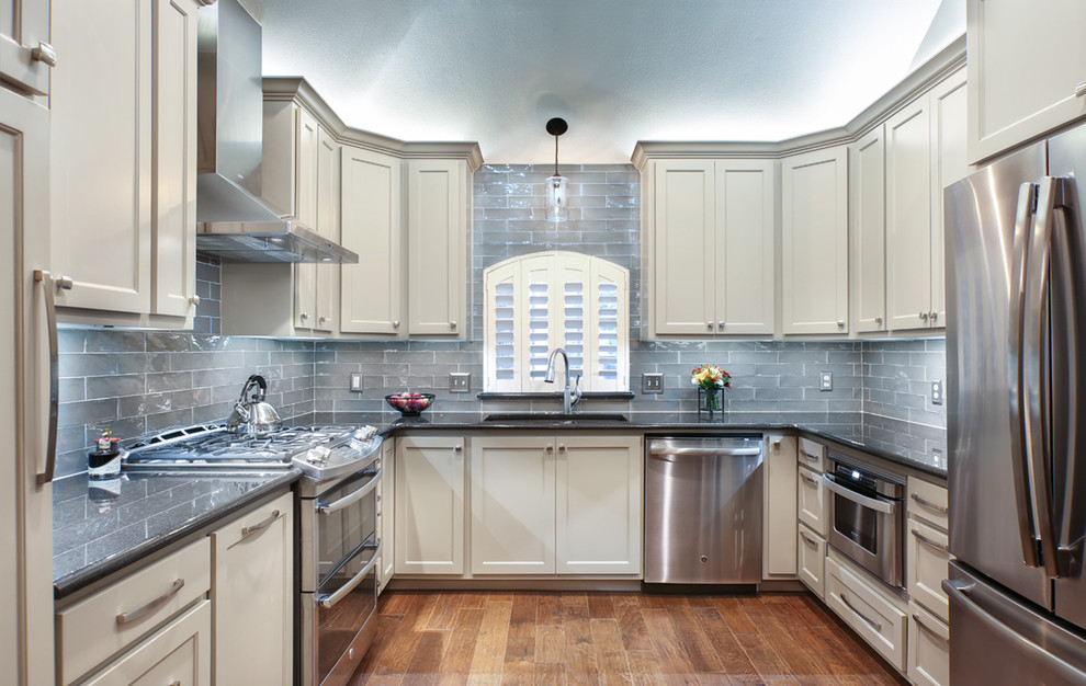 Small minimalist u-shaped medium tone wood floor enclosed kitchen photo with an undermount sink, recessed-panel cabinets, beige cabinets, granite countertops, blue backsplash, glass tile backsplash, stainless steel appliances and no island