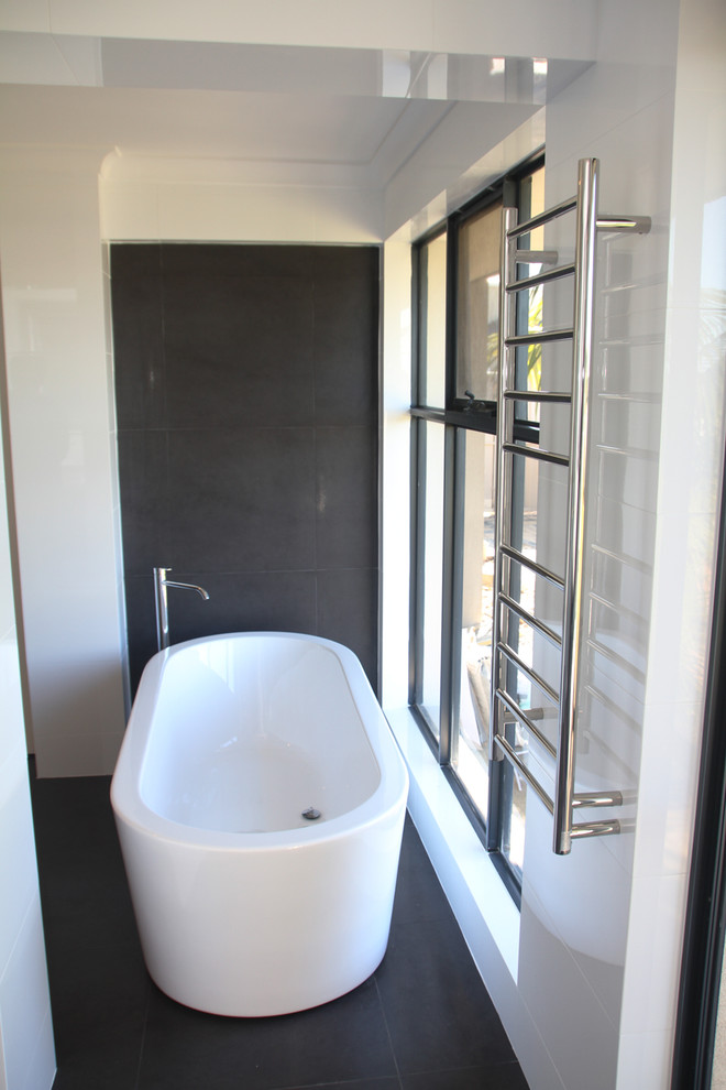 Cette photo montre une très grande salle de bain chic avec des portes de placard blanches, une baignoire indépendante, un carrelage noir et un mur blanc.