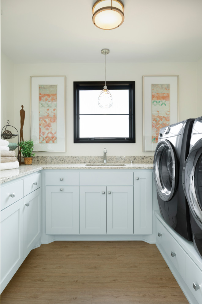 Idéer för att renovera en stor vintage beige u-formad beige tvättstuga enbart för tvätt, med en undermonterad diskho, släta luckor, vita skåp, granitbänkskiva, vita väggar, vinylgolv, en tvättmaskin och torktumlare bredvid varandra och brunt golv