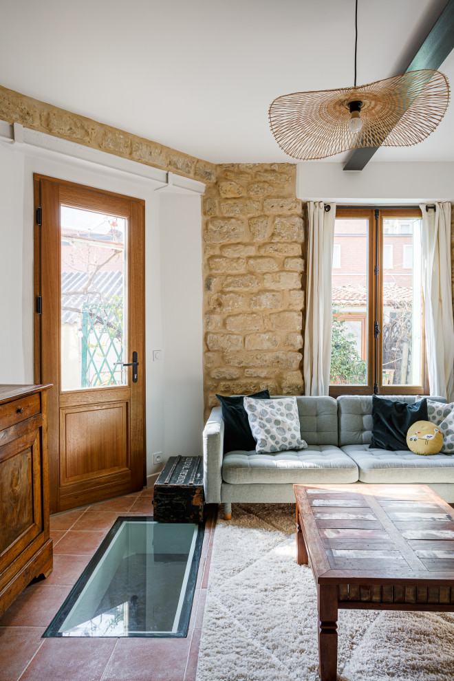 На фото: гостиная комната среднего размера в стиле кантри с бежевыми стенами, полом из терракотовой плитки и балками на потолке с
