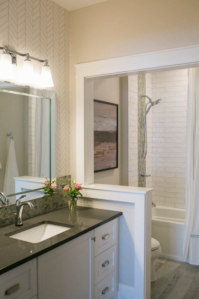 This is an example of a mid-sized traditional bathroom in Other with shaker cabinets, white cabinets, an alcove tub, a shower/bathtub combo, multi-coloured tile, glass tile, beige walls, porcelain floors, an undermount sink, engineered quartz benchtops, grey floor, a shower curtain, grey benchtops and a two-piece toilet.