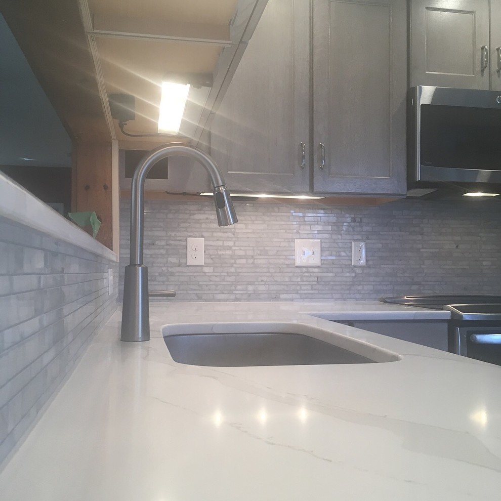 Example of a mid-sized transitional u-shaped kitchen design in Boston with an undermount sink, recessed-panel cabinets, gray cabinets, quartzite countertops, gray backsplash, stone tile backsplash, stainless steel appliances, no island and white countertops