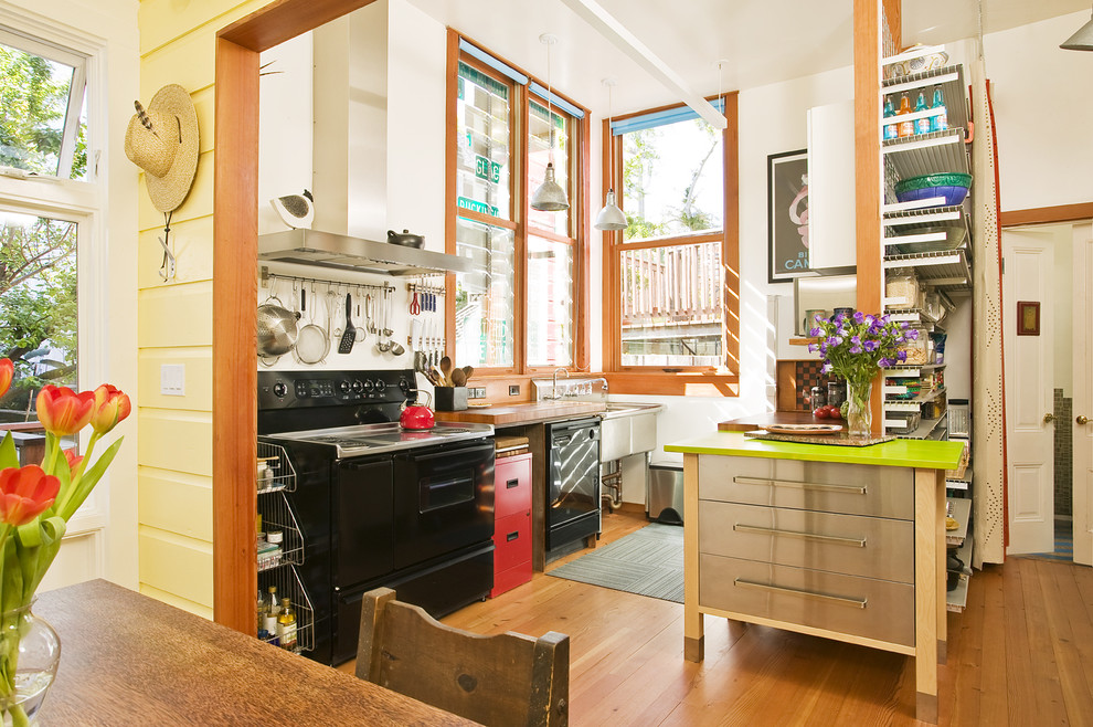 Inspiration for a small midcentury single-wall eat-in kitchen in San Francisco with a farmhouse sink, black appliances, with island, solid surface benchtops, light hardwood floors and beige floor.