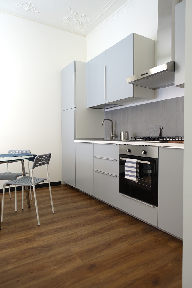 Design ideas for a mid-sized contemporary single-wall separate kitchen in Other with a drop-in sink, flat-panel cabinets, grey cabinets, laminate benchtops, grey splashback, porcelain splashback, laminate floors, no island, grey benchtop, panelled appliances and brown floor.