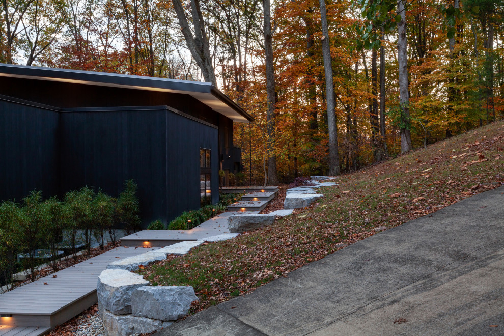This is an example of a mid-sized modern two-storey black house exterior in Indianapolis with wood siding, a shed roof, a metal roof, a grey roof and board and batten siding.