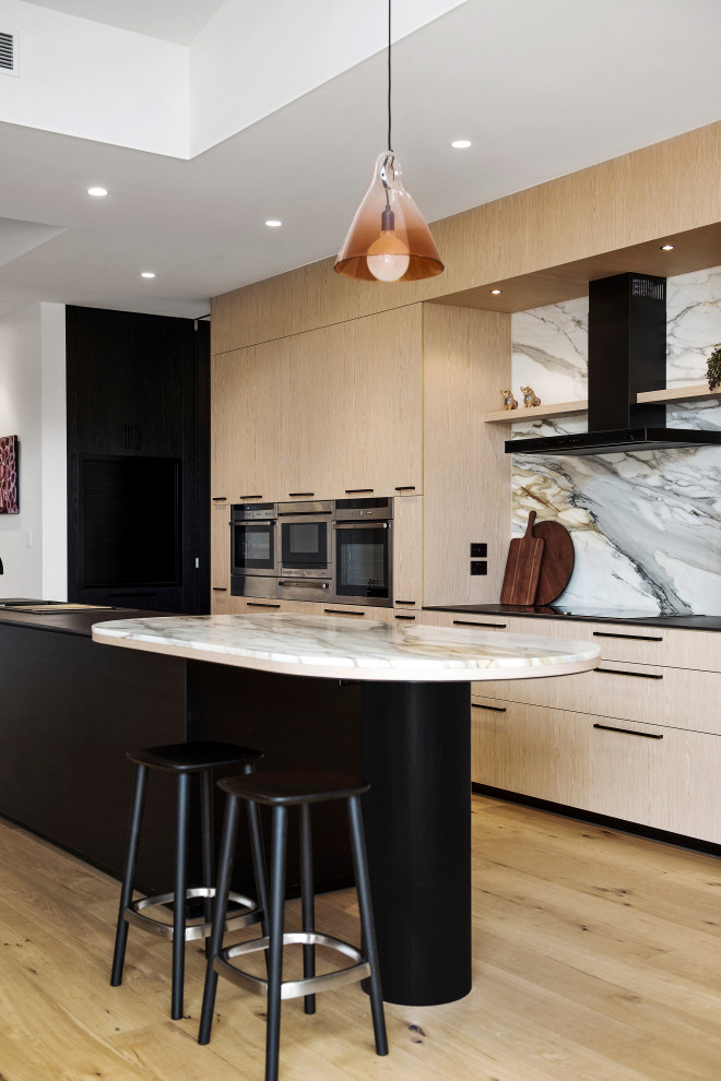 Design ideas for a large contemporary galley kitchen in Adelaide with flat-panel cabinets, light wood cabinets, grey splashback, stainless steel appliances, light hardwood floors, with island, beige floor and black benchtop.