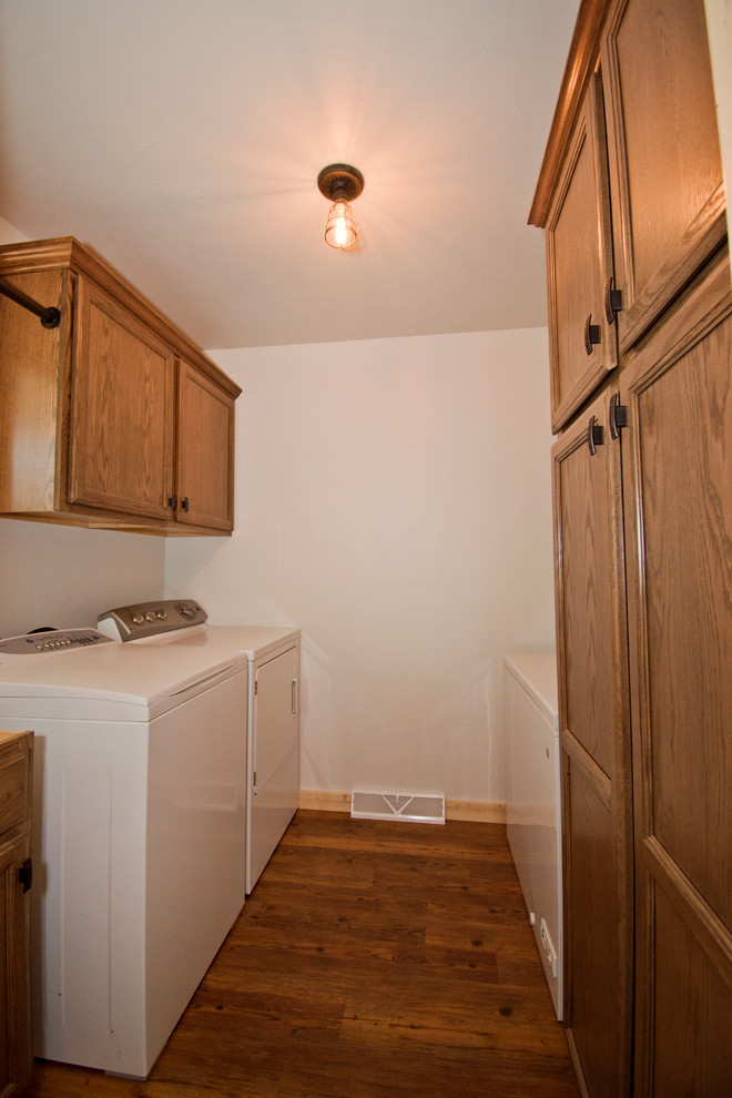 Example of a mid-sized mountain style galley medium tone wood floor and brown floor dedicated laundry room design with recessed-panel cabinets, brown cabinets, white walls and a side-by-side washer/dryer