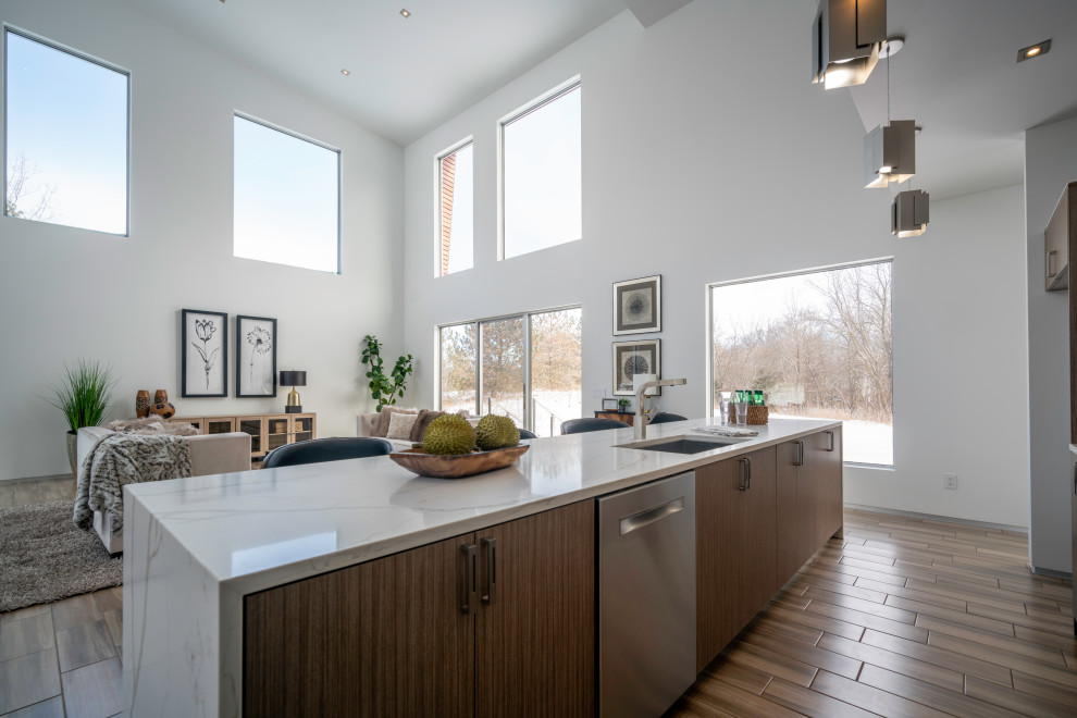 This is an example of a large scandinavian galley open plan kitchen in Detroit with an undermount sink, flat-panel cabinets, light wood cabinets, quartz benchtops, white splashback, stone slab splashback, stainless steel appliances, porcelain floors, with island, brown floor and white benchtop.