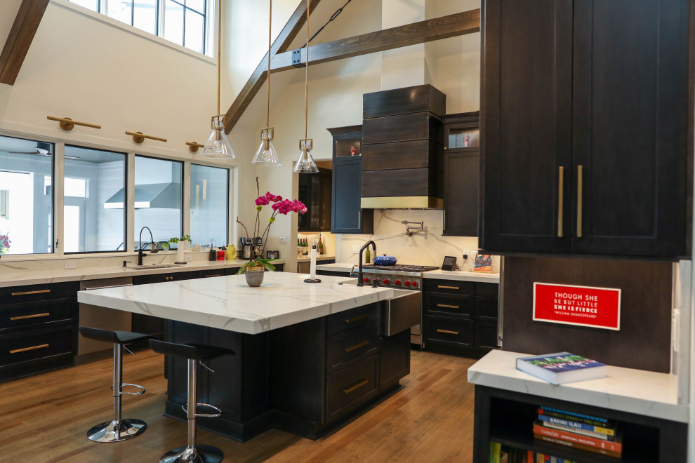 Large transitional u-shaped light wood floor open concept kitchen photo with a farmhouse sink, flat-panel cabinets, dark wood cabinets, quartz countertops, white backsplash, quartz backsplash, stainless steel appliances, an island and white countertops