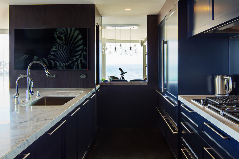 This is an example of a large contemporary galley open plan kitchen in Sydney with an undermount sink, shaker cabinets, blue cabinets, marble benchtops, mirror splashback, stainless steel appliances, dark hardwood floors, with island and black floor.