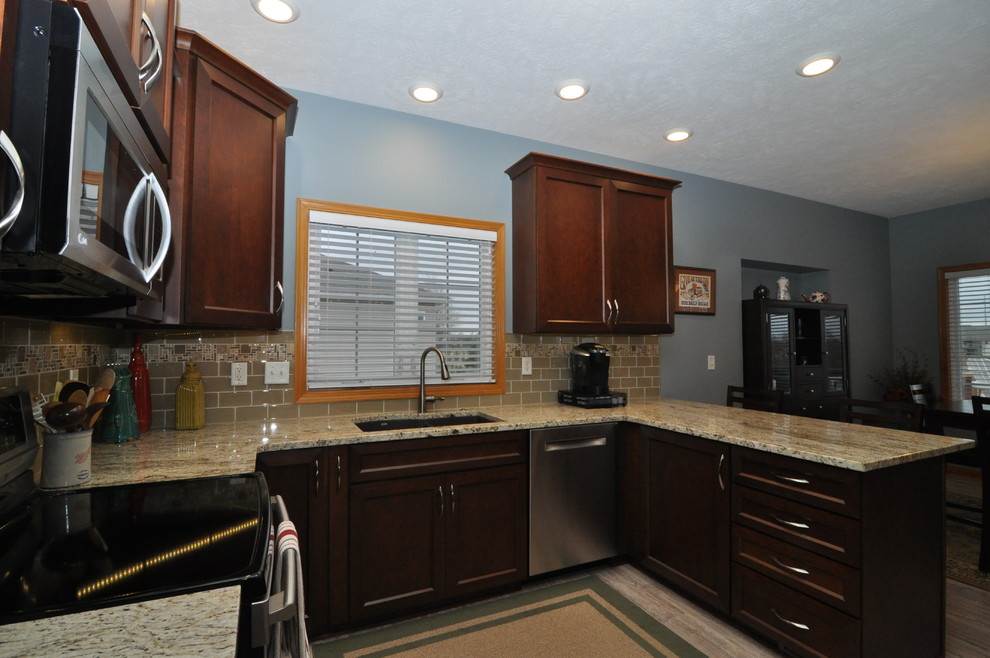 Mid-sized transitional u-shaped porcelain tile eat-in kitchen photo with an undermount sink, recessed-panel cabinets, dark wood cabinets, granite countertops, beige backsplash and stainless steel appliances