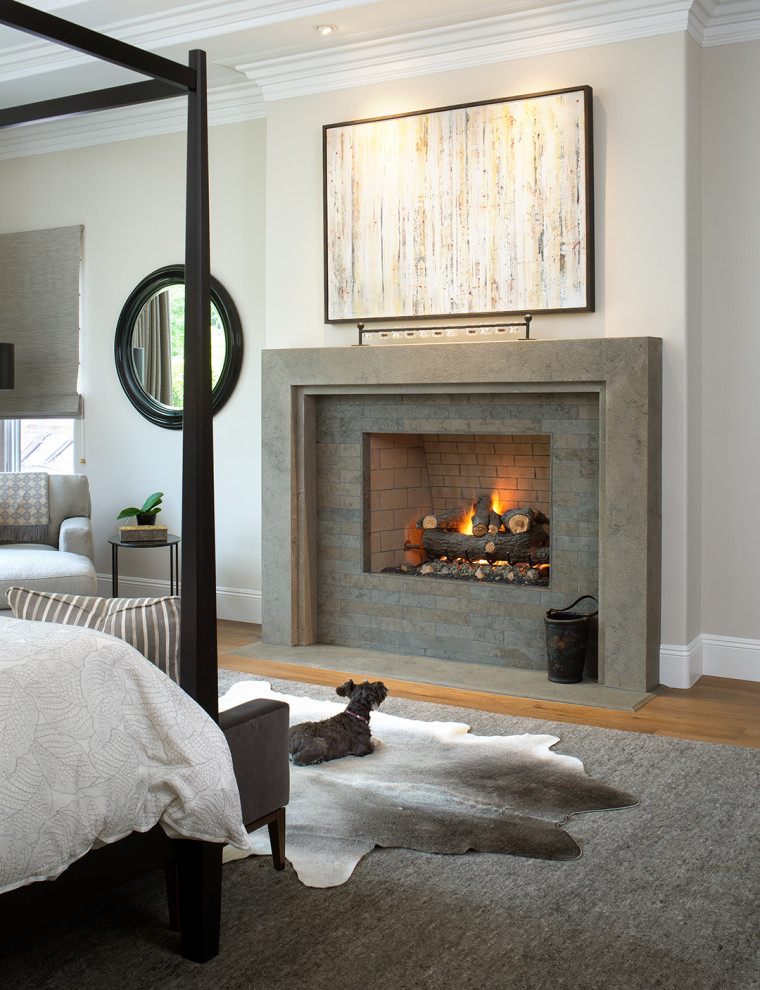 Cette image montre une grande chambre parentale design avec une cheminée standard, un manteau de cheminée en pierre, un mur gris et parquet clair.