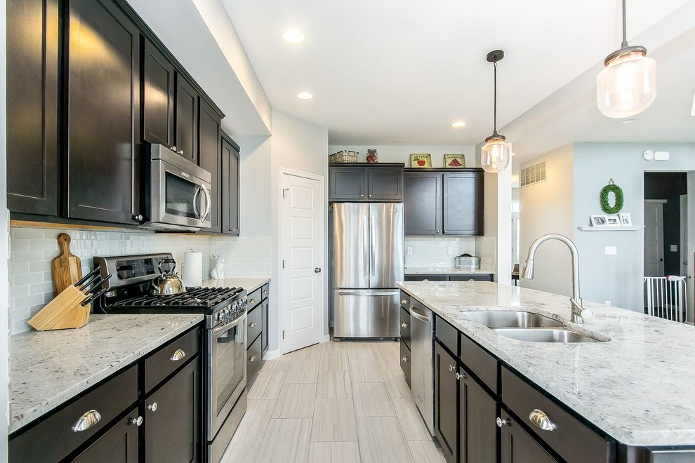 Example of a mid-sized transitional l-shaped porcelain tile and beige floor open concept kitchen design in Columbus with a double-bowl sink, shaker cabinets, dark wood cabinets, granite countertops, white backsplash, glass tile backsplash, stainless steel appliances and an island